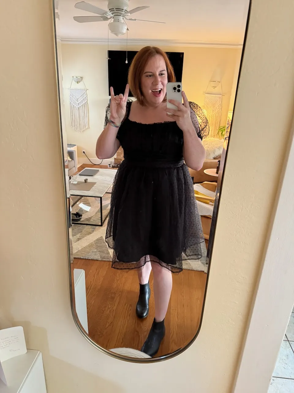 A woman standing in front of a mirror wearing a black dress with her hands in the shape of a fox