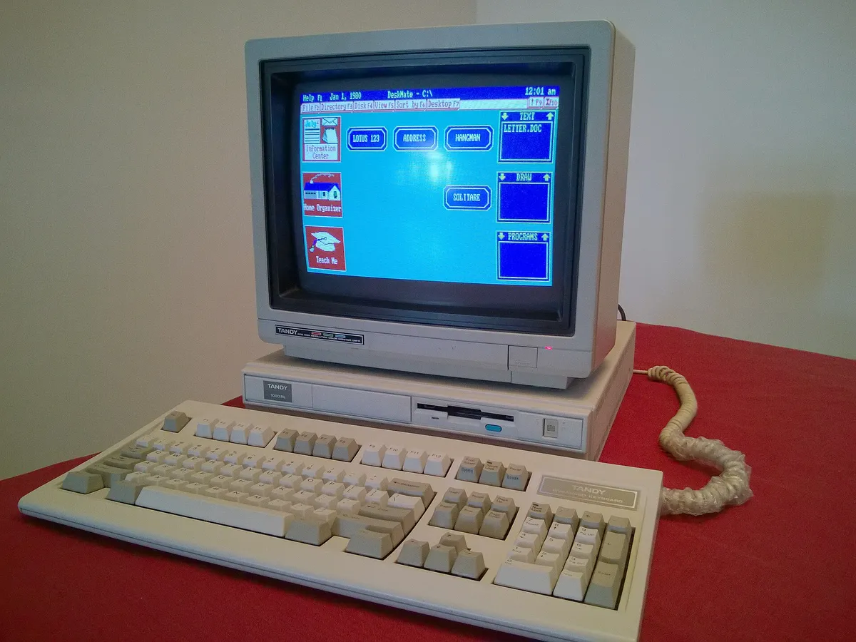 Tandy 1000 RL computer with monitor showing the DeskMate desktop, keyboard, and floppy drive
