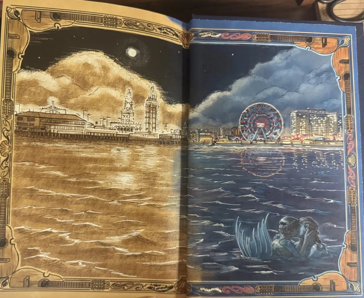 A two-page illustration of the Coney Island skyline with the ocean below it. The left side of the illustration is in sepia tones, featuring a brightly glowing moon in the cloudy sky. The right side of the illustration is colored in shades of deep blue for the sea and gold for the glowing lights of the ferris wheel and amusement park attractions. In the lower right corner, Benny and Rio share a kiss in the ocean, with Rio's fin visible above the water. The image is bordered with art-deco inspired images of the cuatro, a ten-stringed Caribbean instrument.