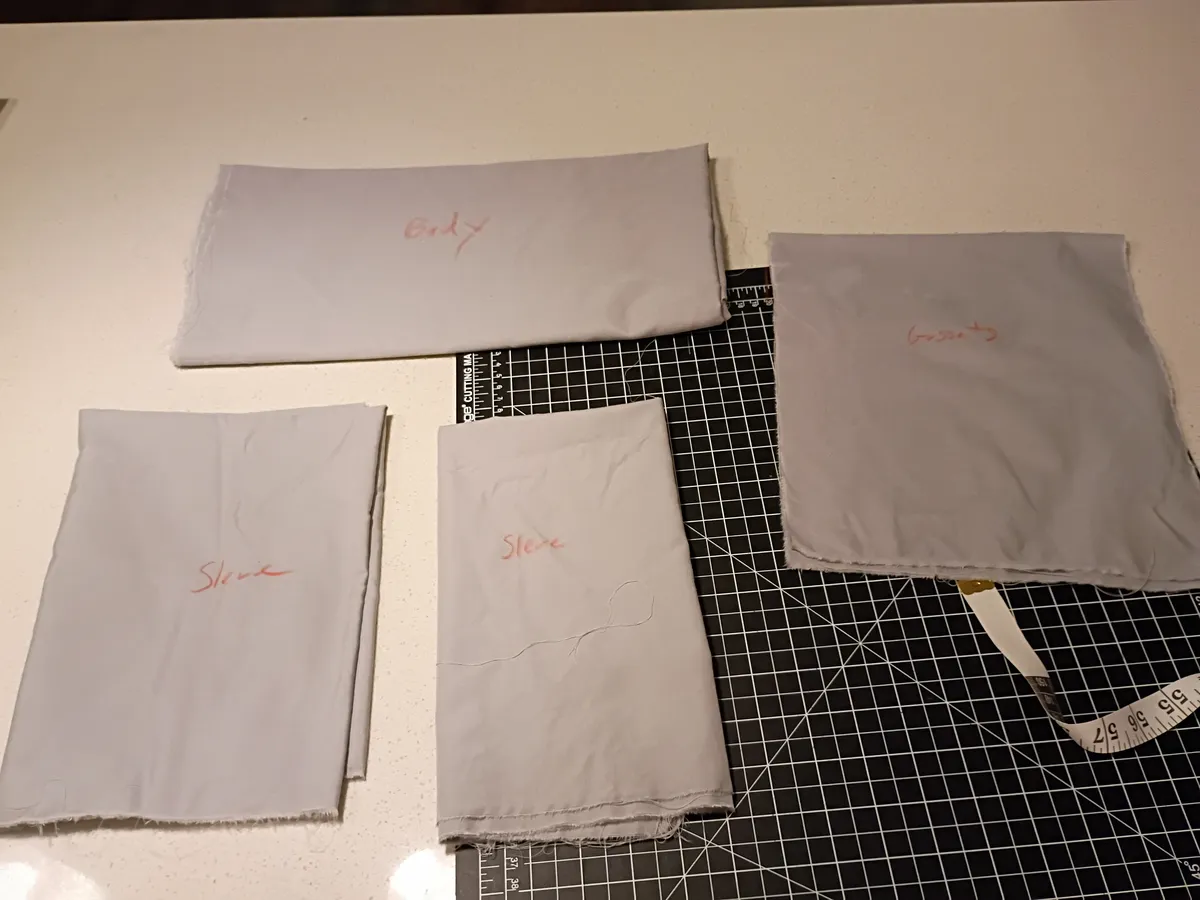 Photo of shirt parts in blue-grey cotton folded on a cutting mat.