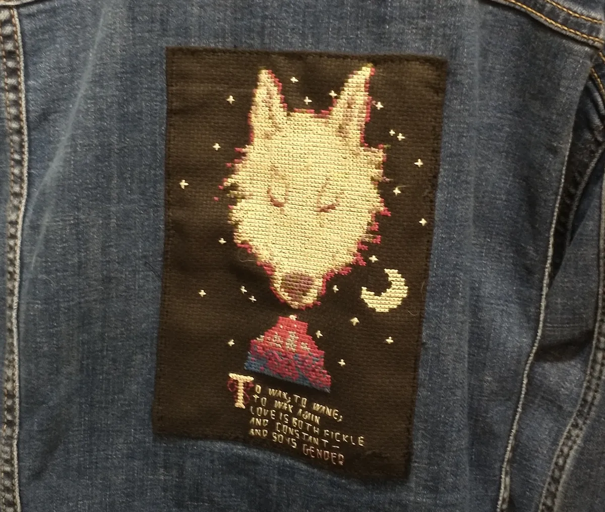 Cross-stitch of a monstrous werewolf with caption "To wax, to wane, to wax again. Love is both fickle and constant, and so is gender"