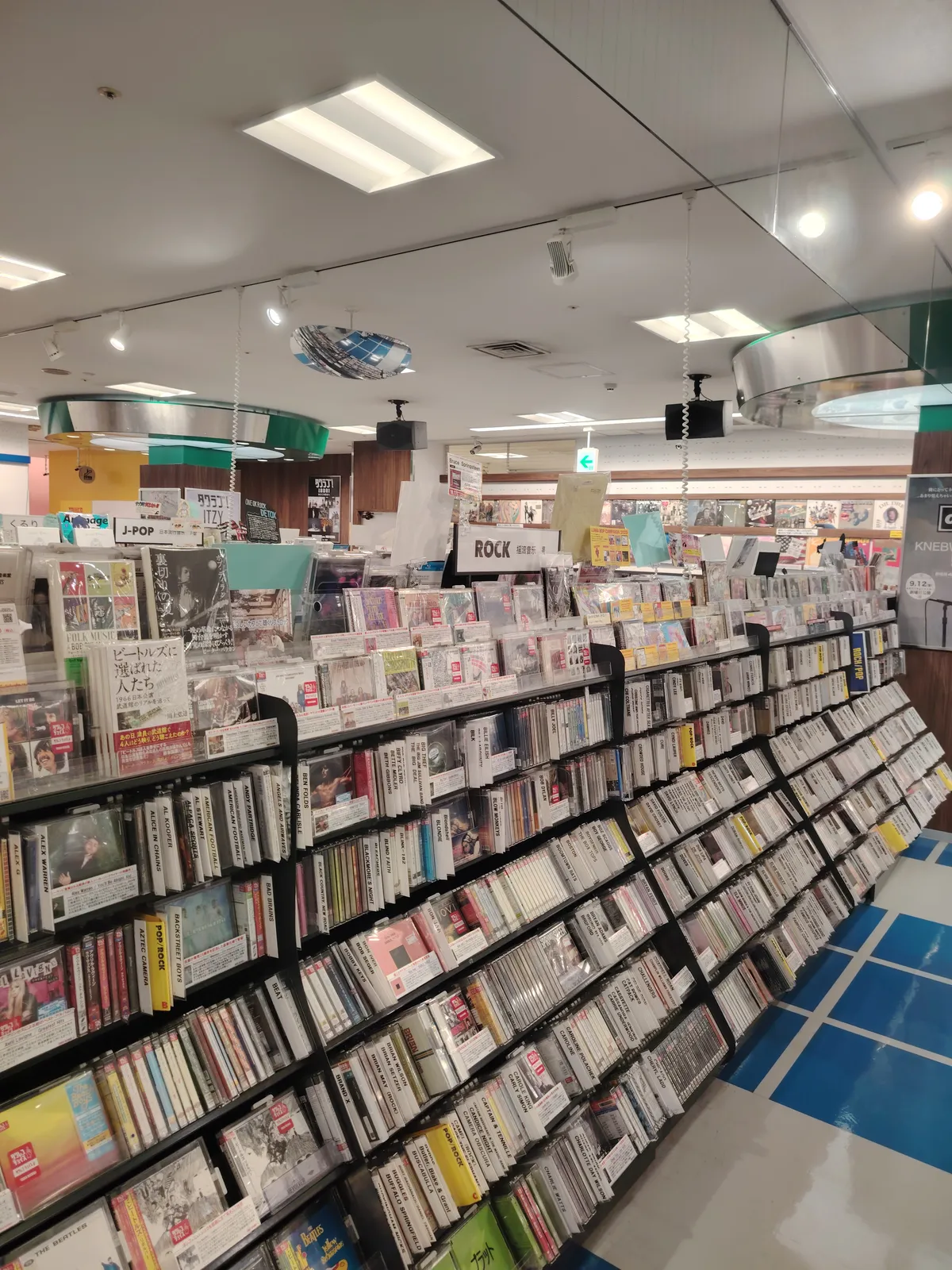 the inside of a tower records store. Hundreds of cds on display shelves, organized by genre.