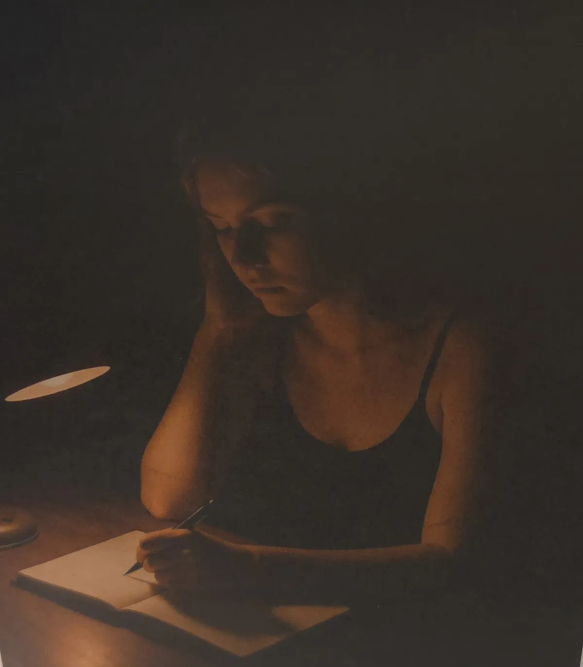 Kendyl writing at her desk, dimly lit by lamp.
