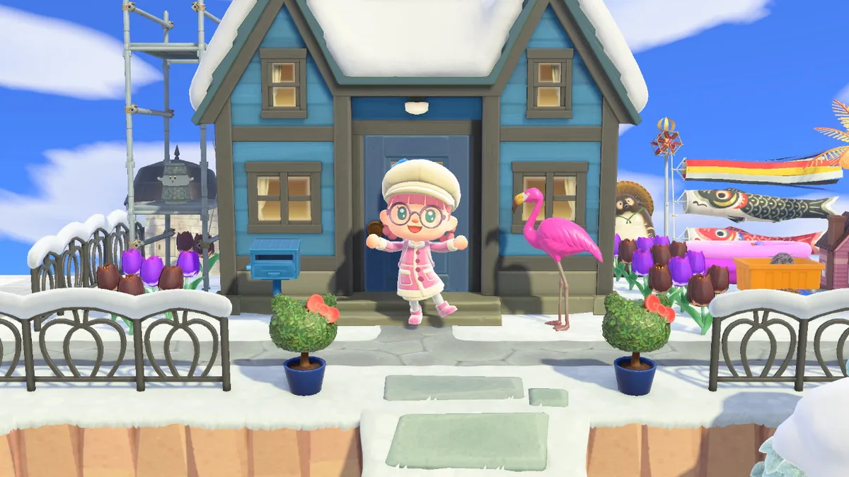 Screenshot from Animal Crossing: New Horizons, showing Slothra, my character, wearing a pink shearling coat, pink shearling boots, and a big white hat, with pink hair and purple glasses, standing in front of a blue house, with Hello Kitty topiary, black and purple tulips, and a plastic flamingo