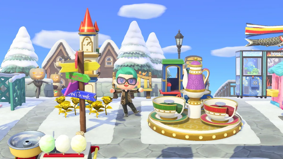 Slothra is standing next to a spinning tea cups ride. There is also a train engine ride behind the tea cups and a clock tower and signpost to the left.