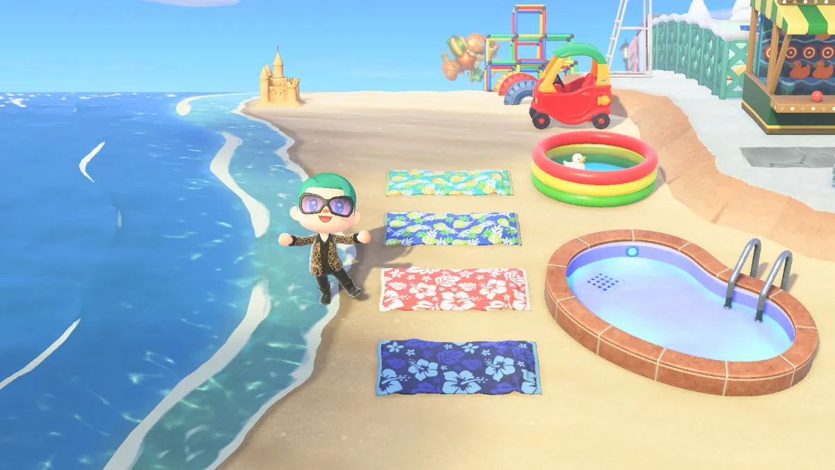 Slothra stands partially in the ocean to show off several beach towels to the right, as well as a plastic kiddie pool and a larger tiled pool.
