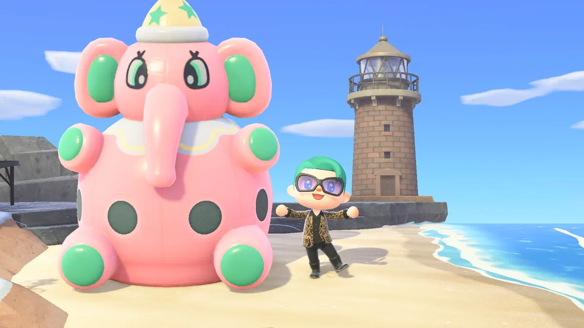 Slothra is standing next to a gigantic pink inflated cartoon elephant. There is also a lighthouse in the back.