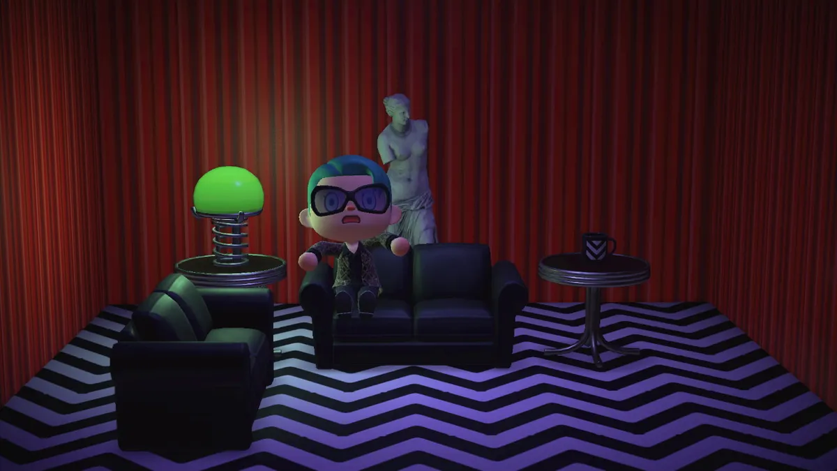 Slothra sits on a black leather sofa in the Red Room from Twin Peaks. There's another black leather sofa, a table with a metal lamp, another table with a single coffee mug, and the Venus de Milo statue behind them.