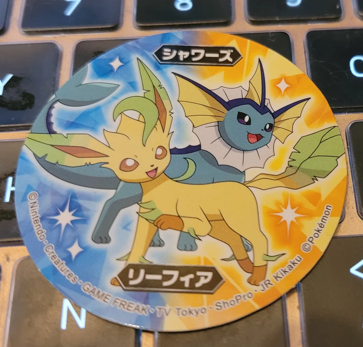A circular sticker with two Pokémon - a Leafon in the front and a Vaporeon in the back.