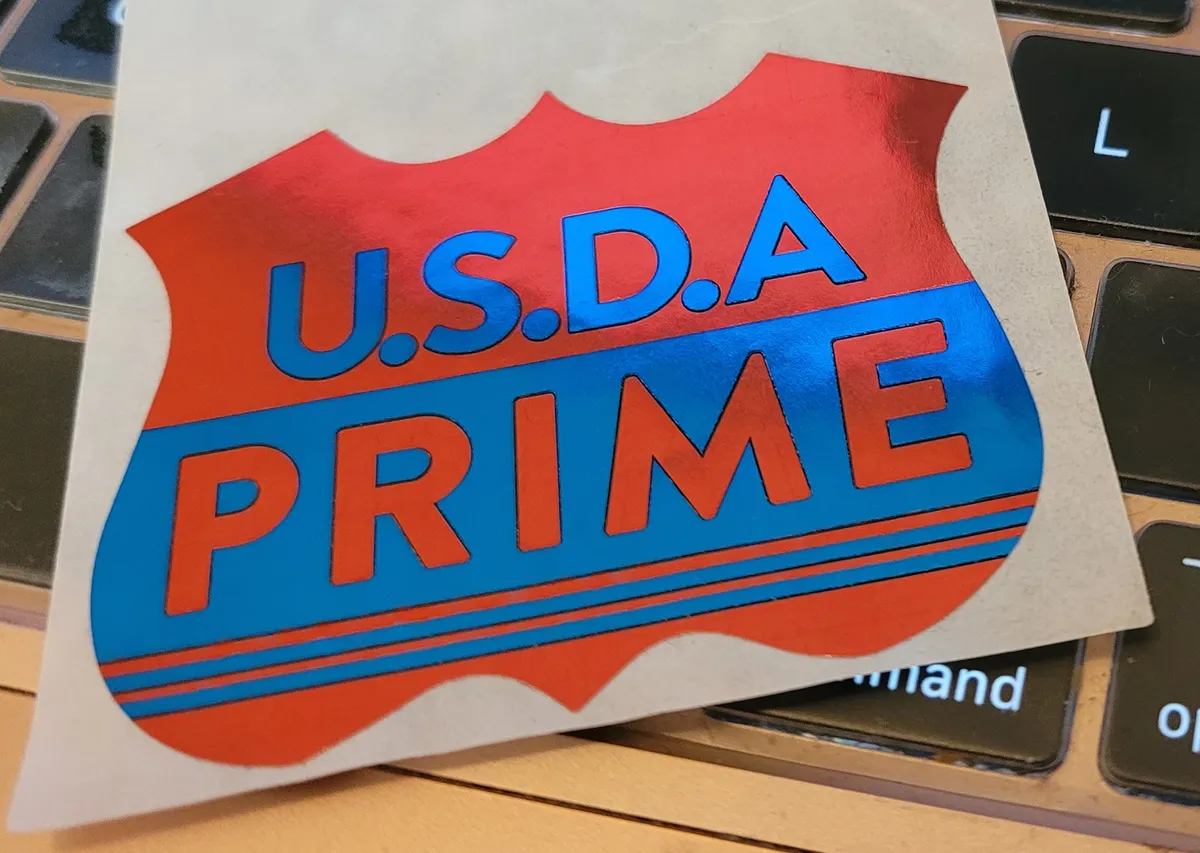 A shiny metallic sticker in the shape of a badge that says on it "USDA PRIME"