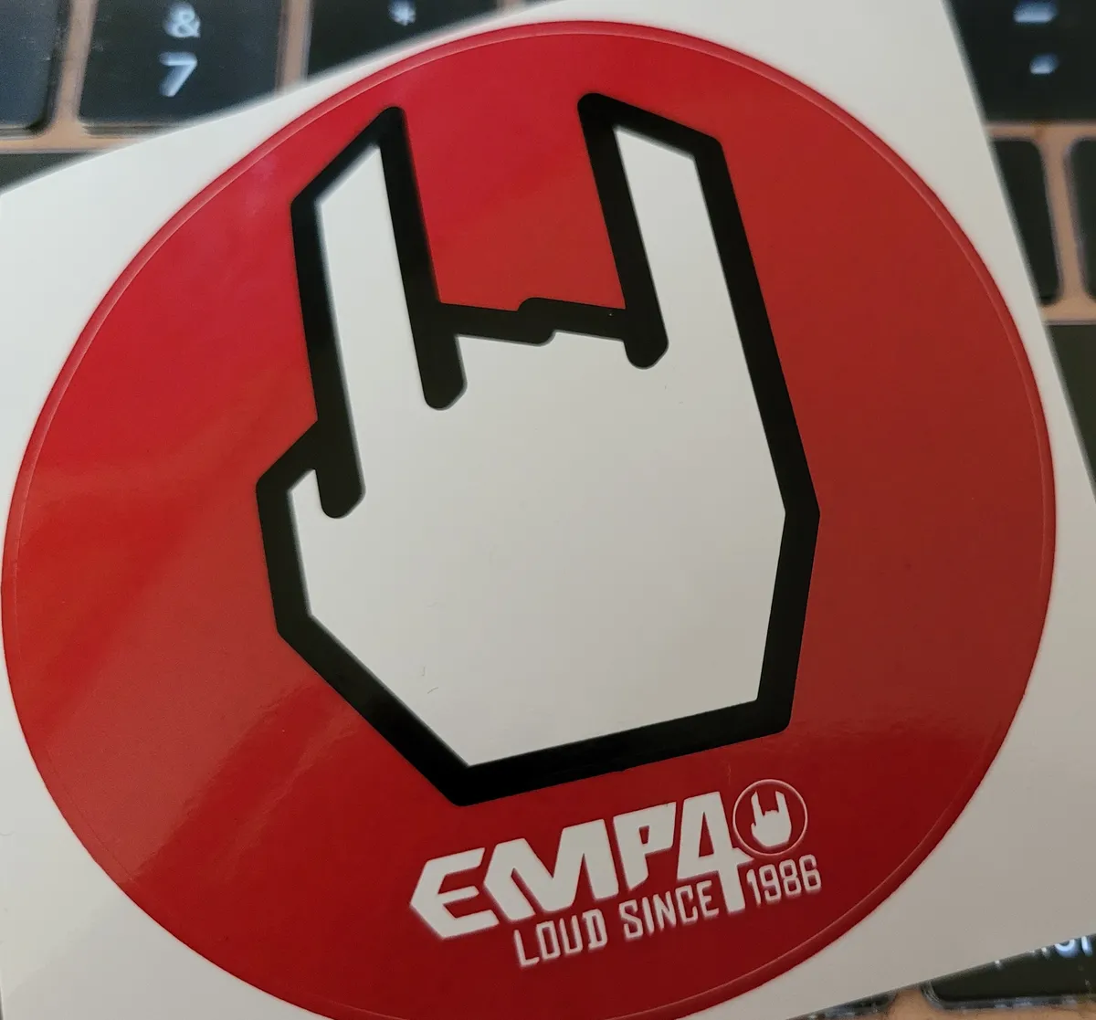 A sticker for the store EMP, which has a hand making the devil's horns gesture.