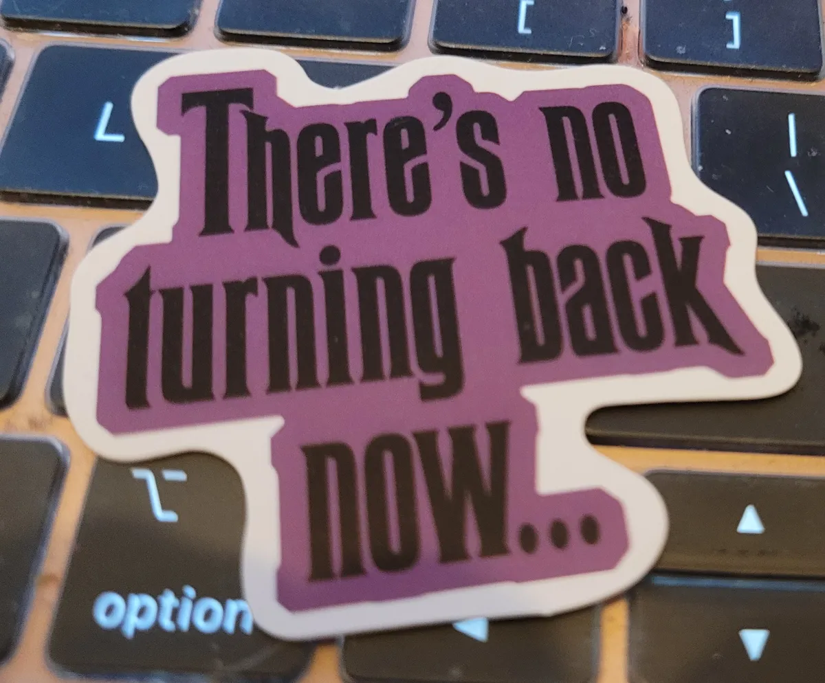 A sticker with black text on a purple background that says "There's no turning back now..." which is from Disneyland's The Haunted Mansion.