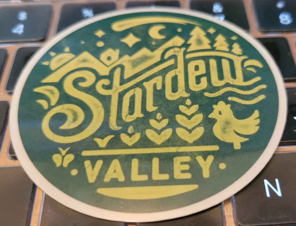 A beautiful round sticker that says Stardew Valley on it, designed to look weather-beaten and faded, with all the things that make Stardew a fantastic pastoral fantasy game - chickens and mountains and trees and crops and a comet in the sky.