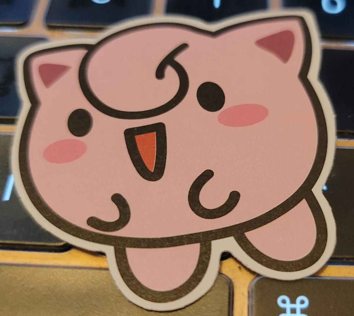 A sticker of a cartoony illustration of a Jigglypuff from Pokémon.