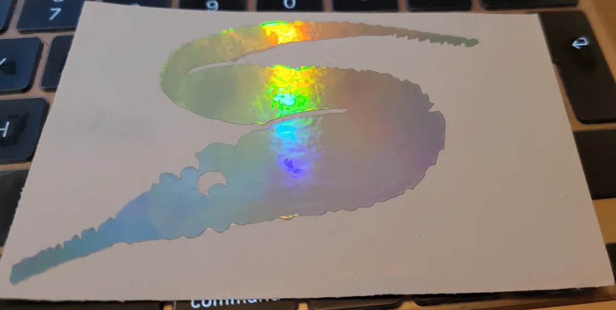 A holographic silver sticker of a fuzzy string worm, the kind you get when you're a kid to do worm tricks.