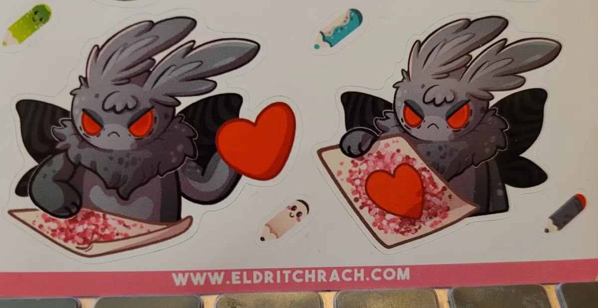 Two stickers of Mothman. In the left one, he is angrily holding up a cardboard heart while his other hand scribbles on a card that is covered in red glitter. In the right one, he has attached the heart to the card and is holding it up. There are also small stickers of pencils around these two bigger stickers – a cactus cat pencil, a Loch Ness Monster pencil, a Fresno nightcrawler pencil, and a Mothman pencil. Underneath all these stickers it says www.eldritchrach.com to remind you where these are from.