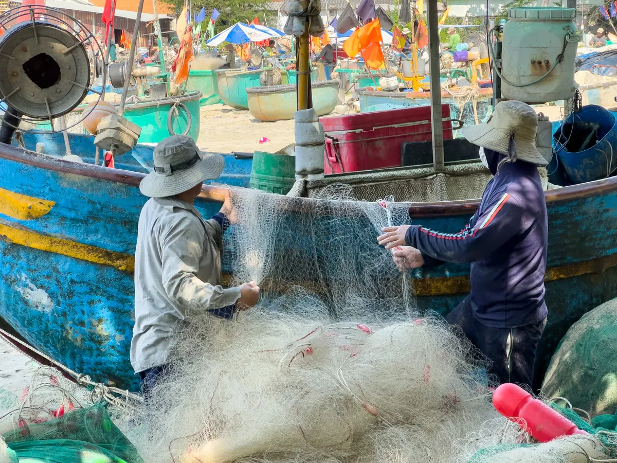 Two fishers detangling their nets and collecting fish and crabs.
