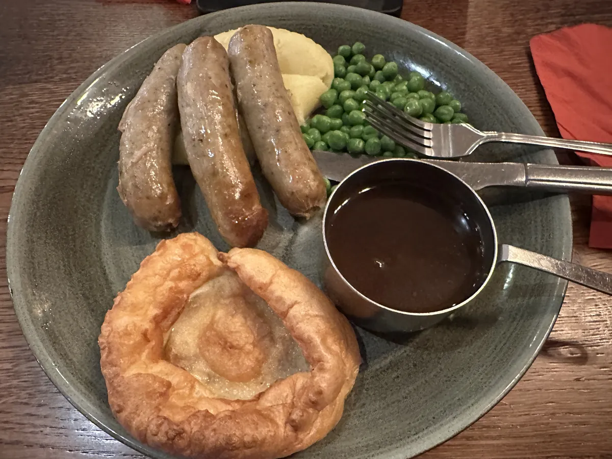 A Scottish breakfast with sausage, mashed potato, green peas, a pastry, and gravy