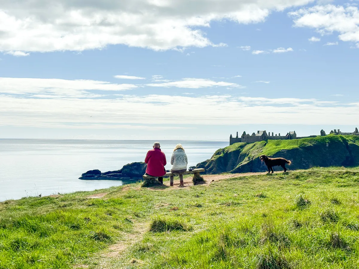 An old couple sitting on a wooden bench, out-looking Dunnottar Castle