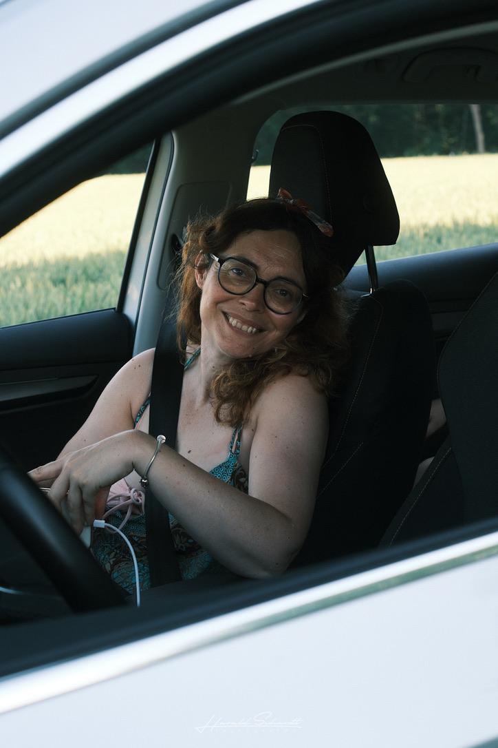 A woman sitting in the passenger seat of a parked car, looking out of the open window.