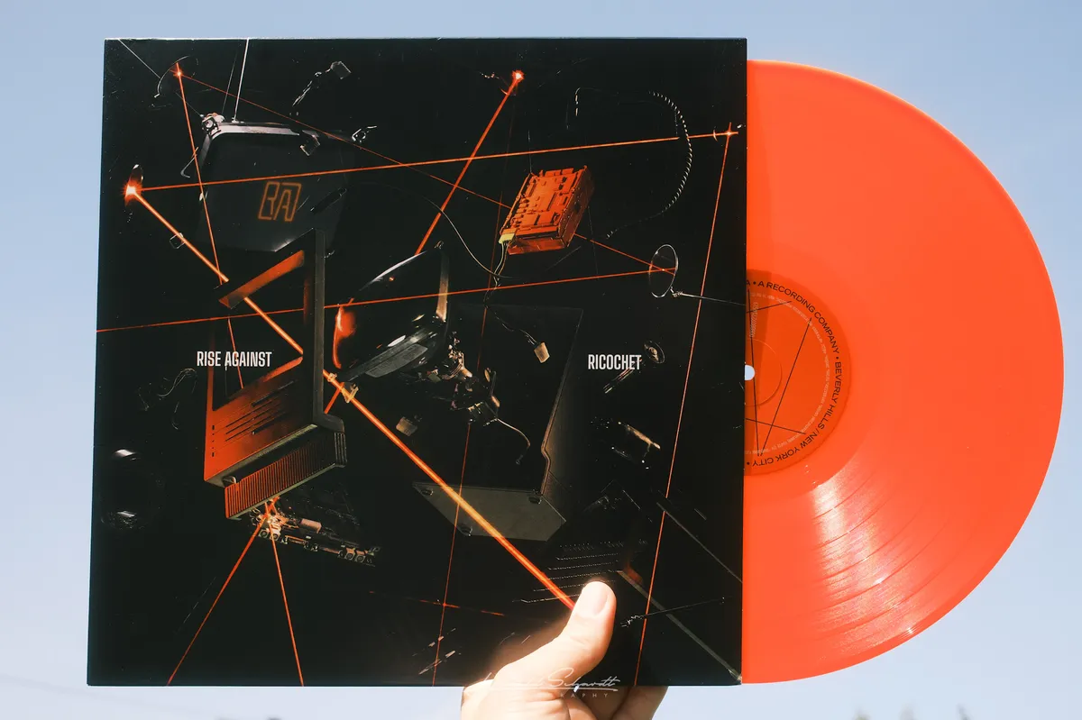 Rise Against — Ricochet, orange vinyl half out of the black sleeve, held against a blue sky.
