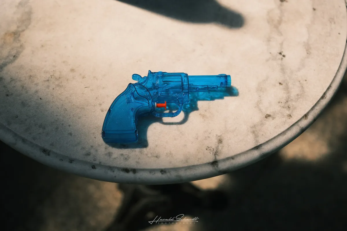 A small transparent blue toy water pistol on a weathered marble table top.