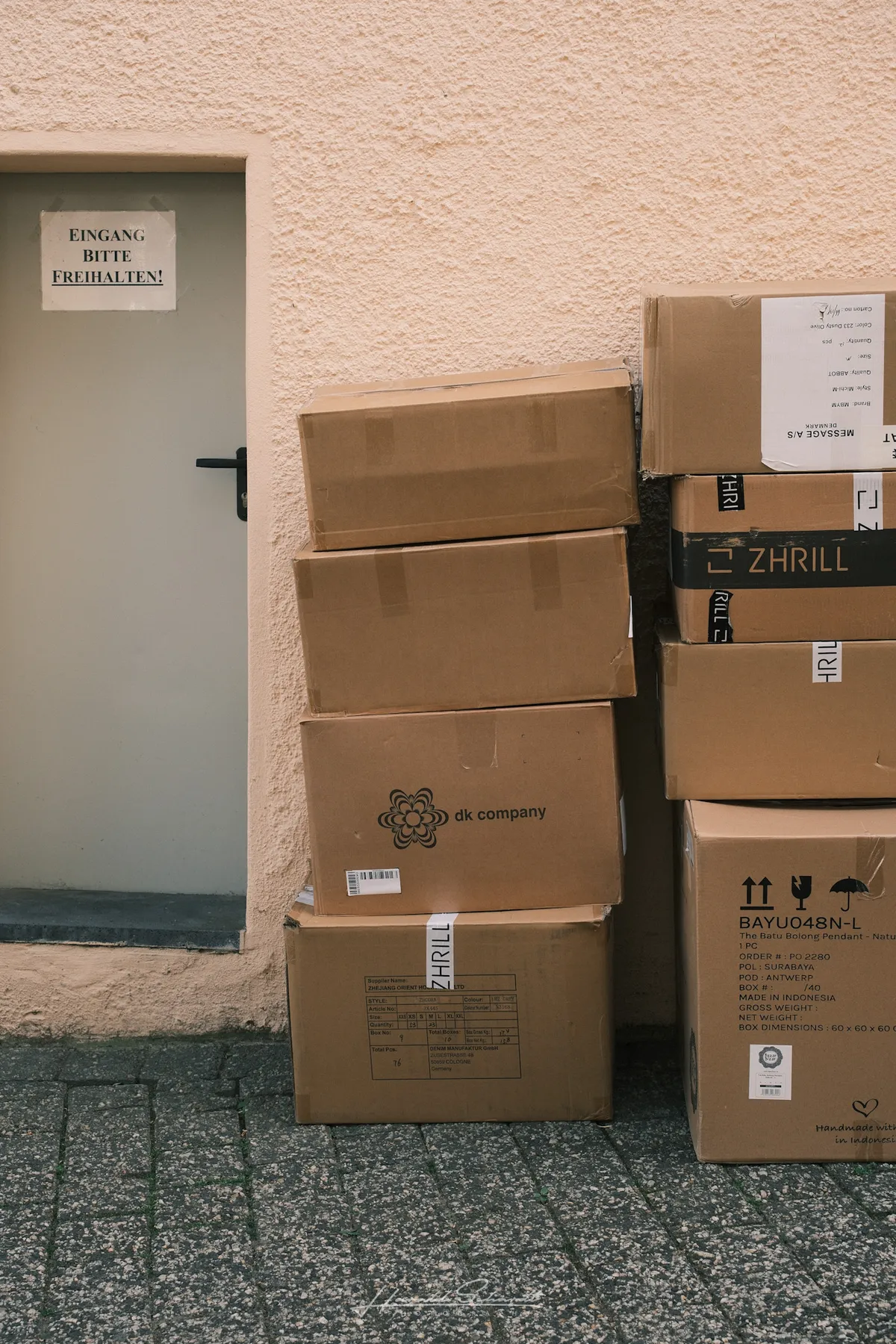 A stack of cardboard delivery boxes leaning against a wall next to a door marked 
