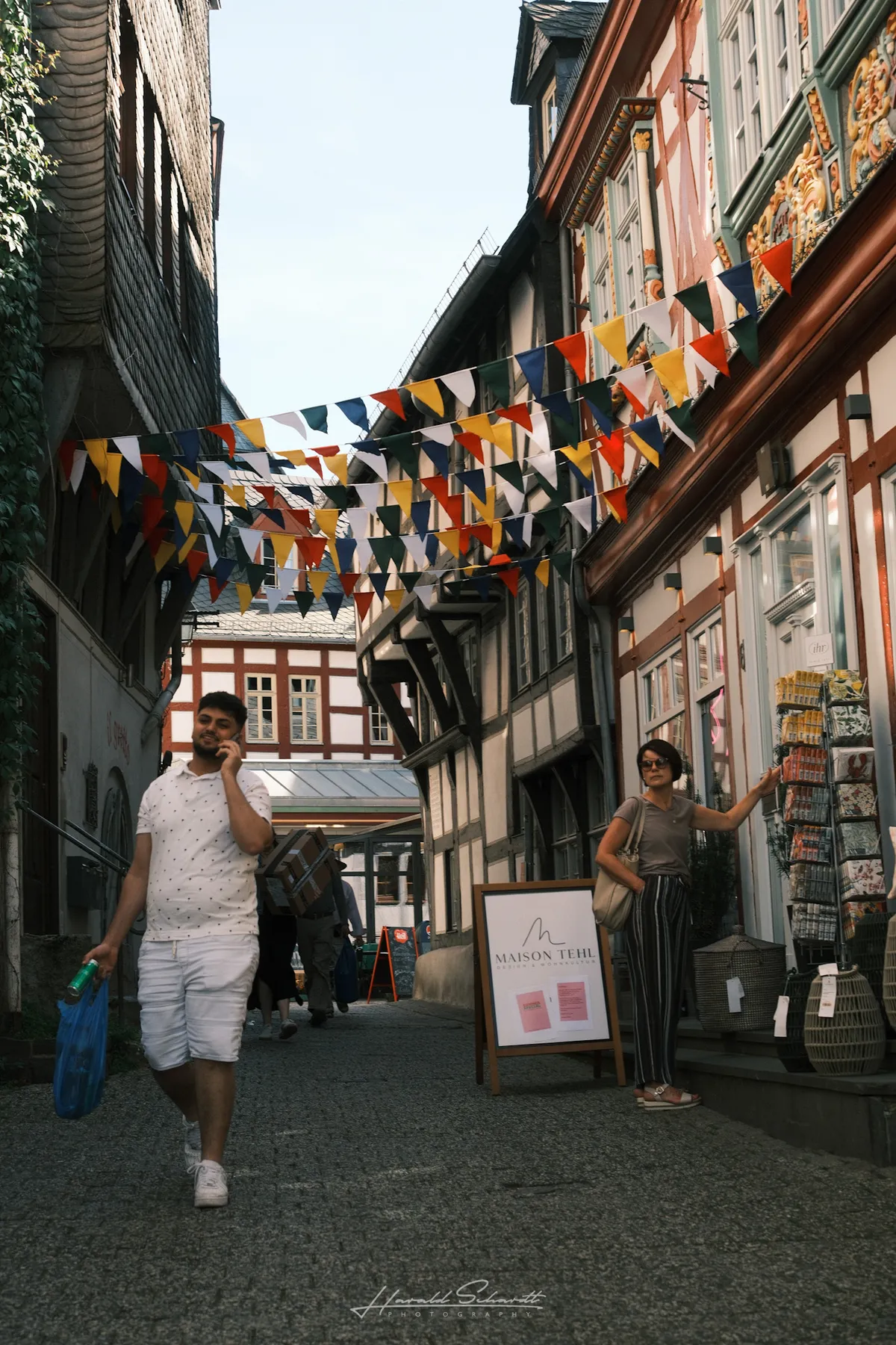 A busy pedestrian street in Limburg old town, colourful bunting strung between half-timbered buildings.