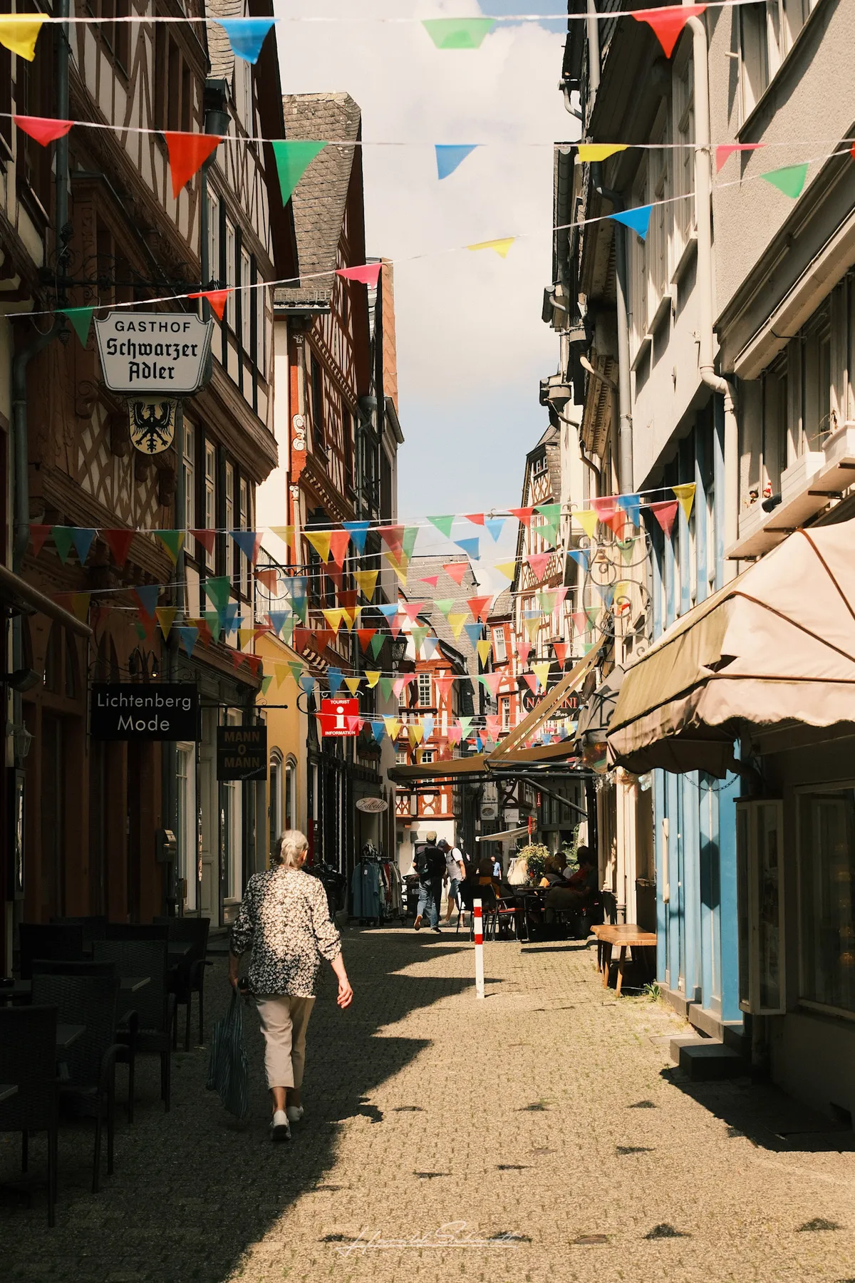 A cobblestone pedestrian street in Limburg old town, colourful bunting strung between half-timbered buildings, a woman walking away from the camera.