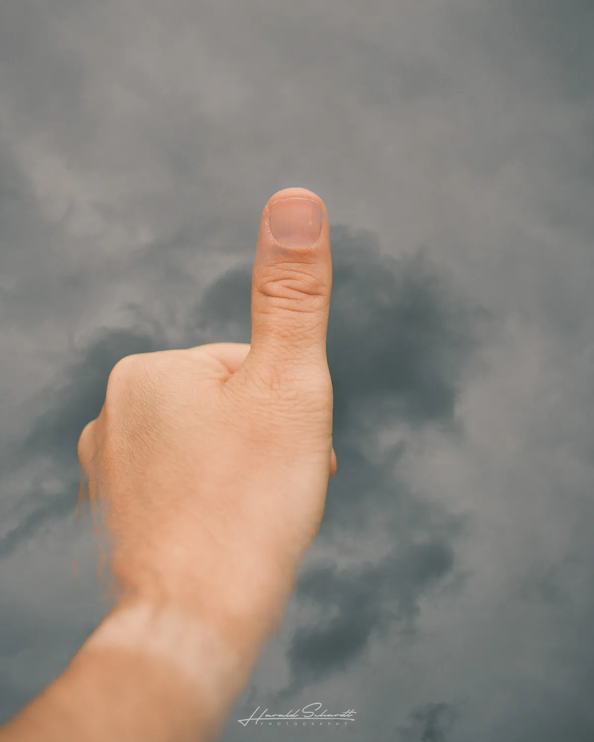 Hand giving a thumbs up against dark storm clouds.