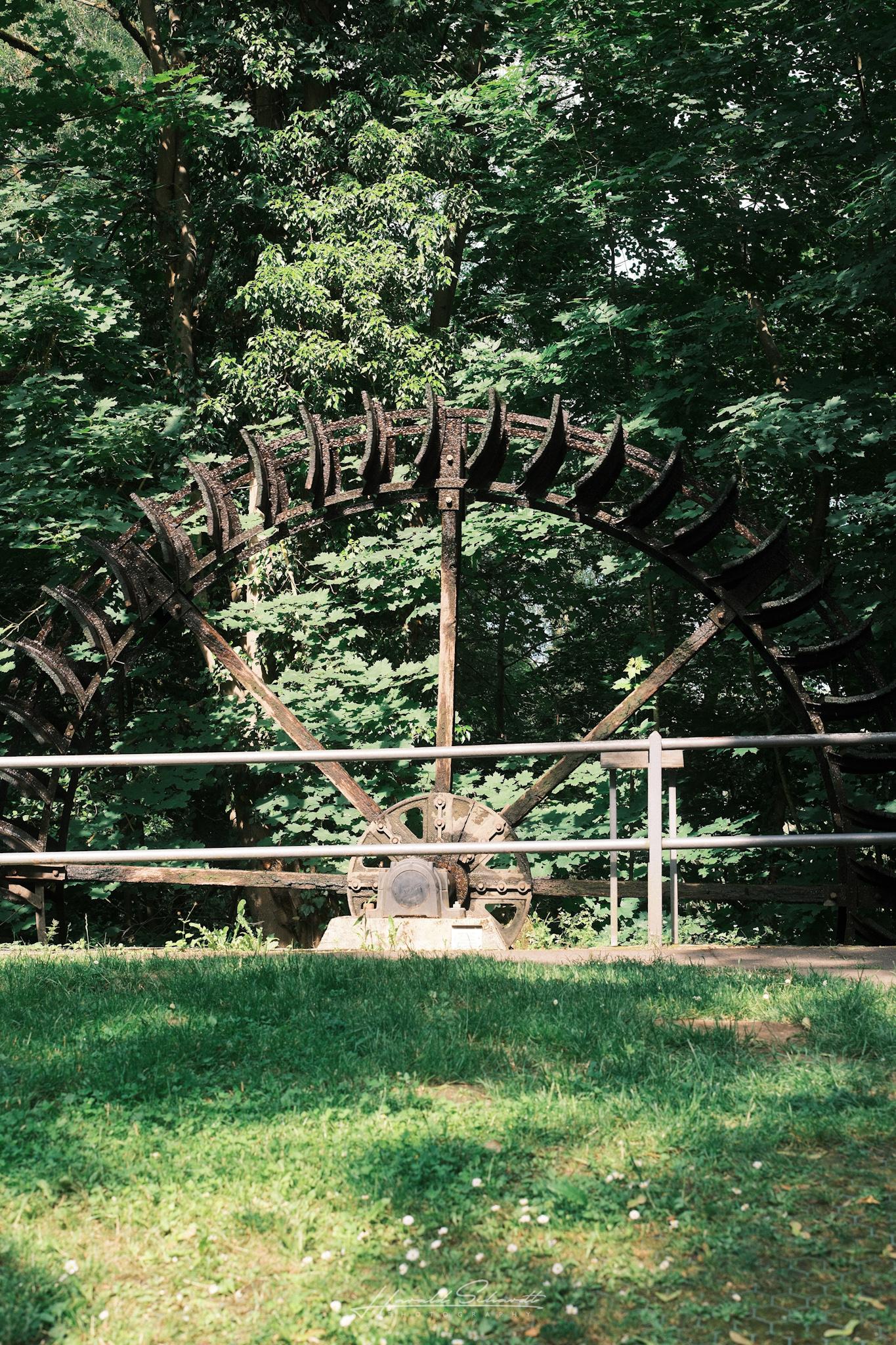 Old water wheel surrounded by greenery in a park-like setting.