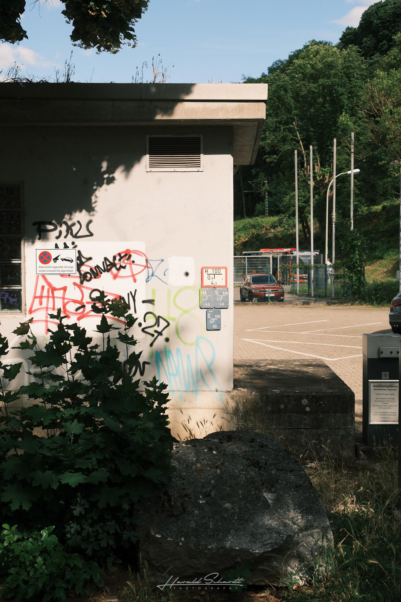 Small building covered in graffiti near the riverside with sunlight and deep shadows.