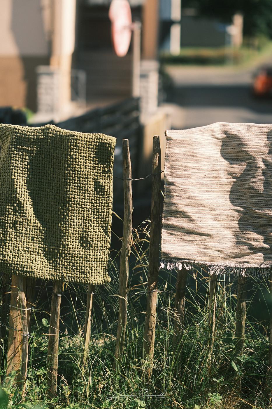 Two towels hanging over a rustic fence in warm summer light, with soft shadows and a blurred garden background.