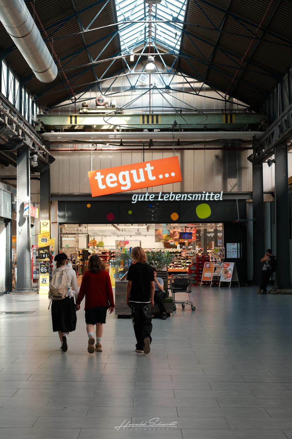 Three people walking past the entrance of a supermarket inside a shopping arcade.