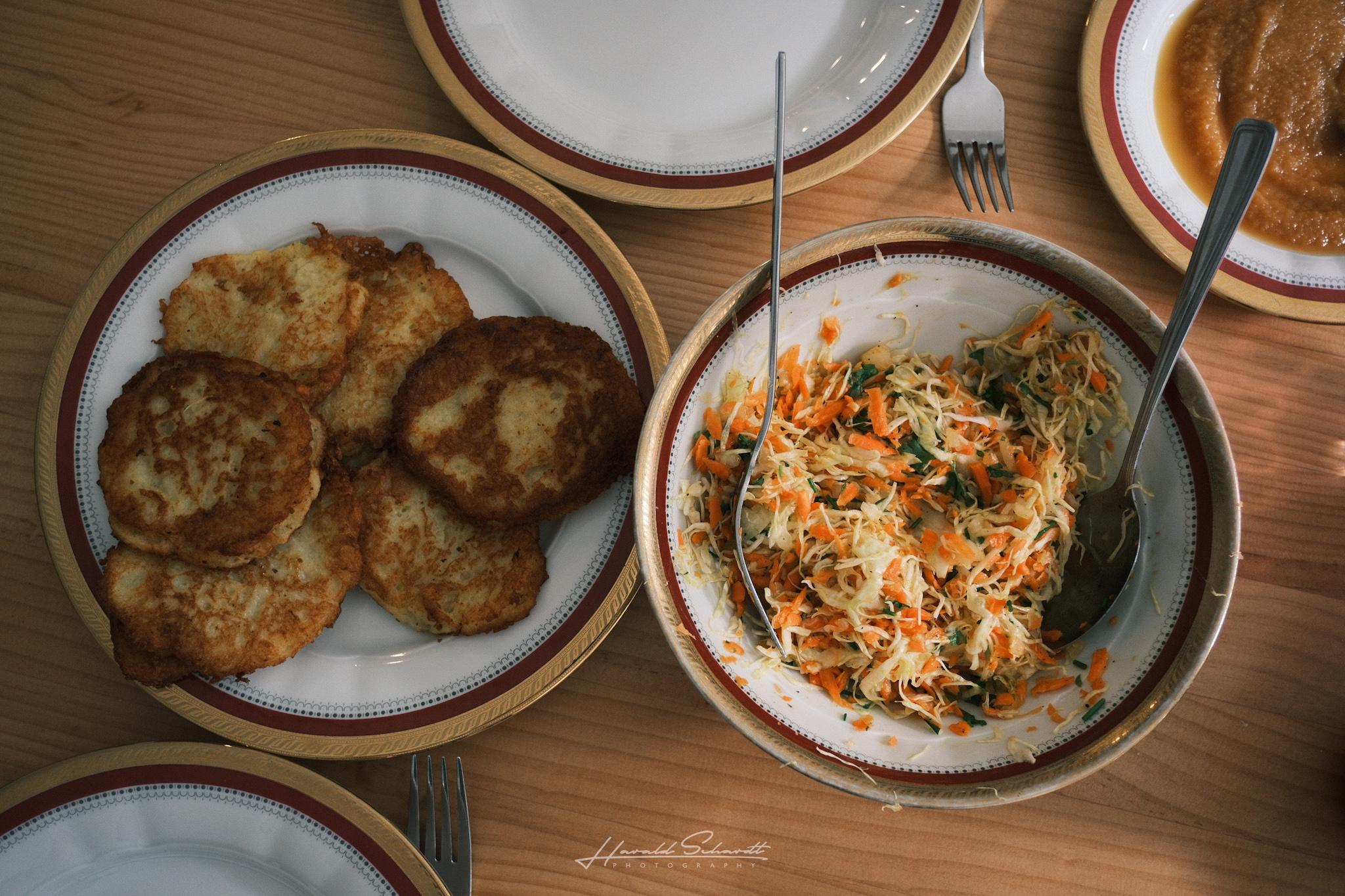Overhead view of a plate with potato pancakes and a bowl of coleslaw.