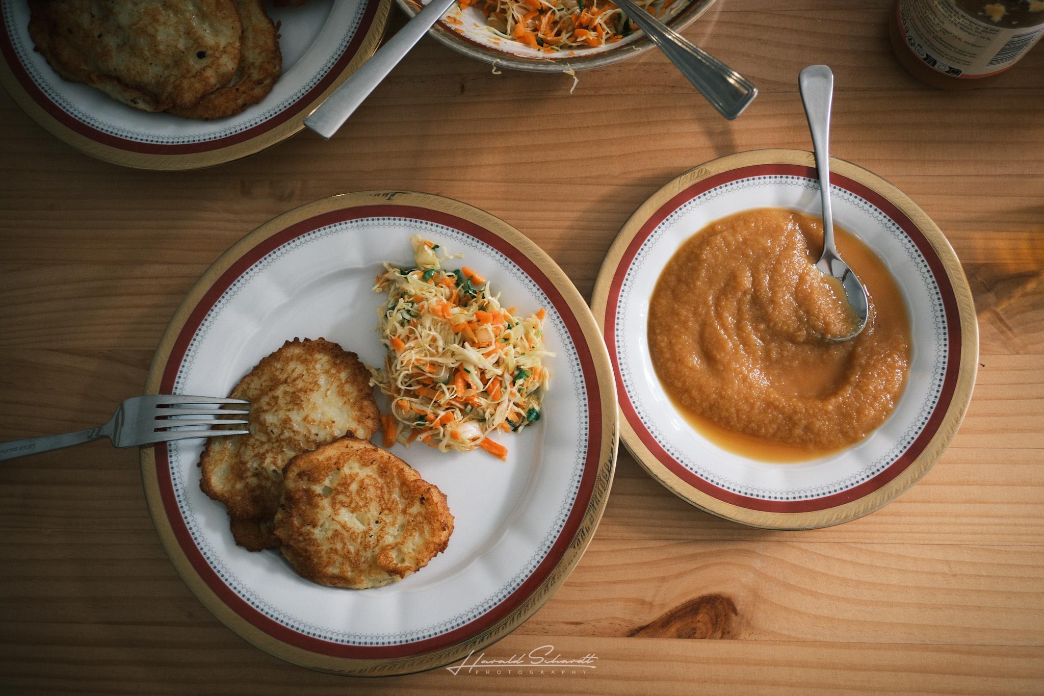 Overhead view of two plates: potato pancakes with coleslaw, and a bowl of applesauce.