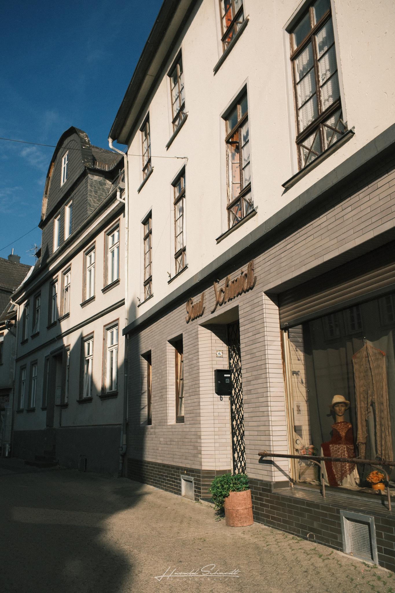 Quiet street with a shop front, mannequin in the display window, old townhouse facades along the road.