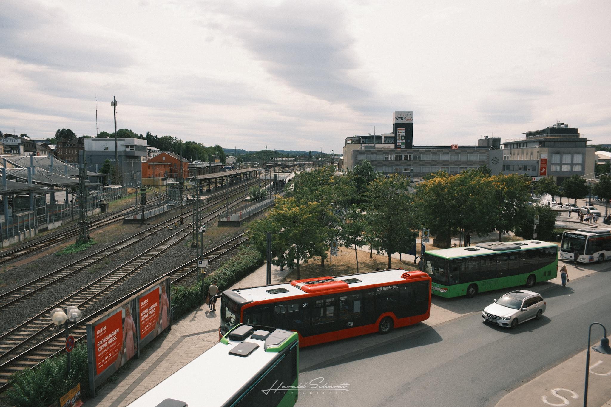 View over Limburg's bus station and railway tracks, with red and green buses waiting below.