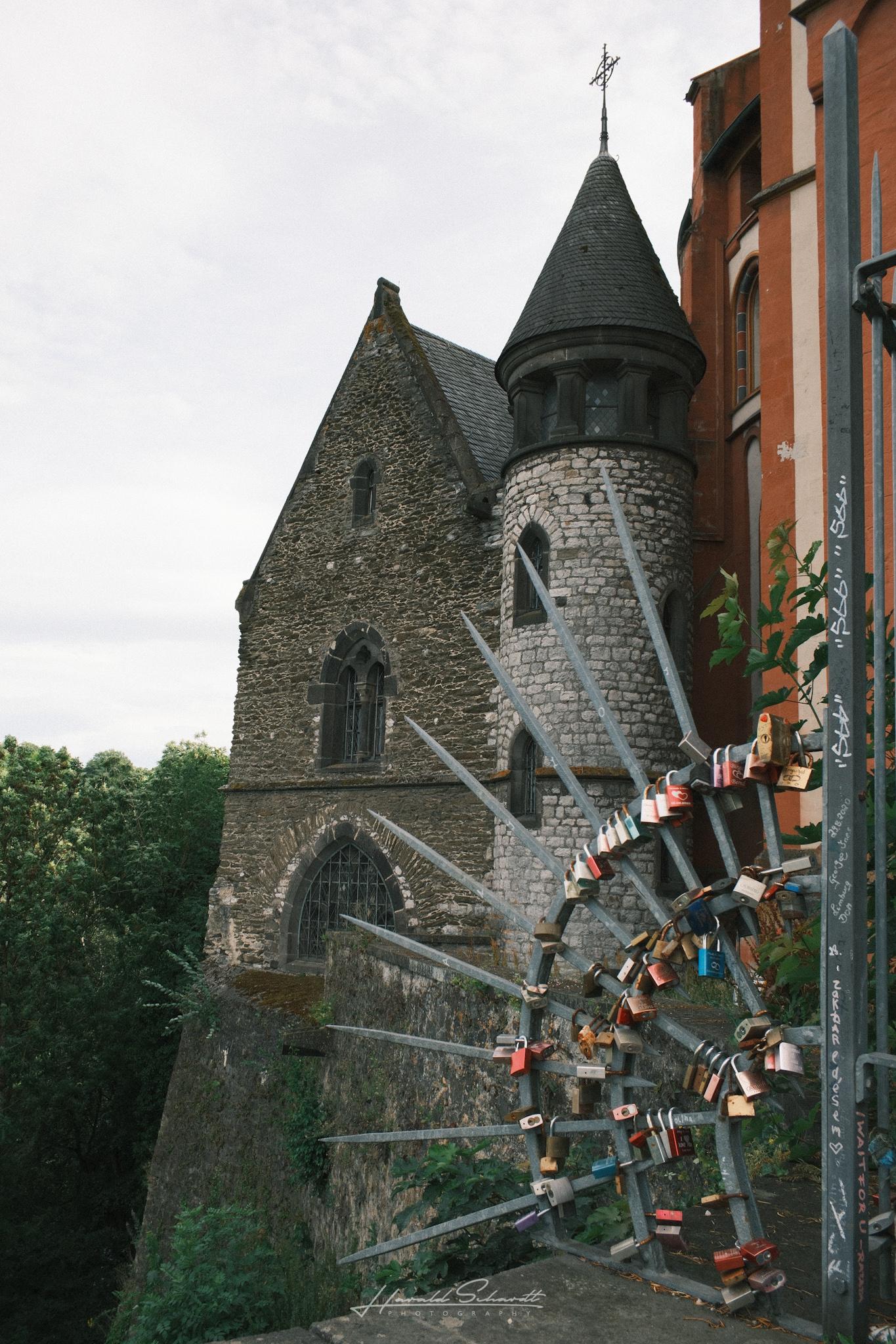 Part of Limburg Castle with its round stone tower, viewed past a railing covered with colorful love locks.