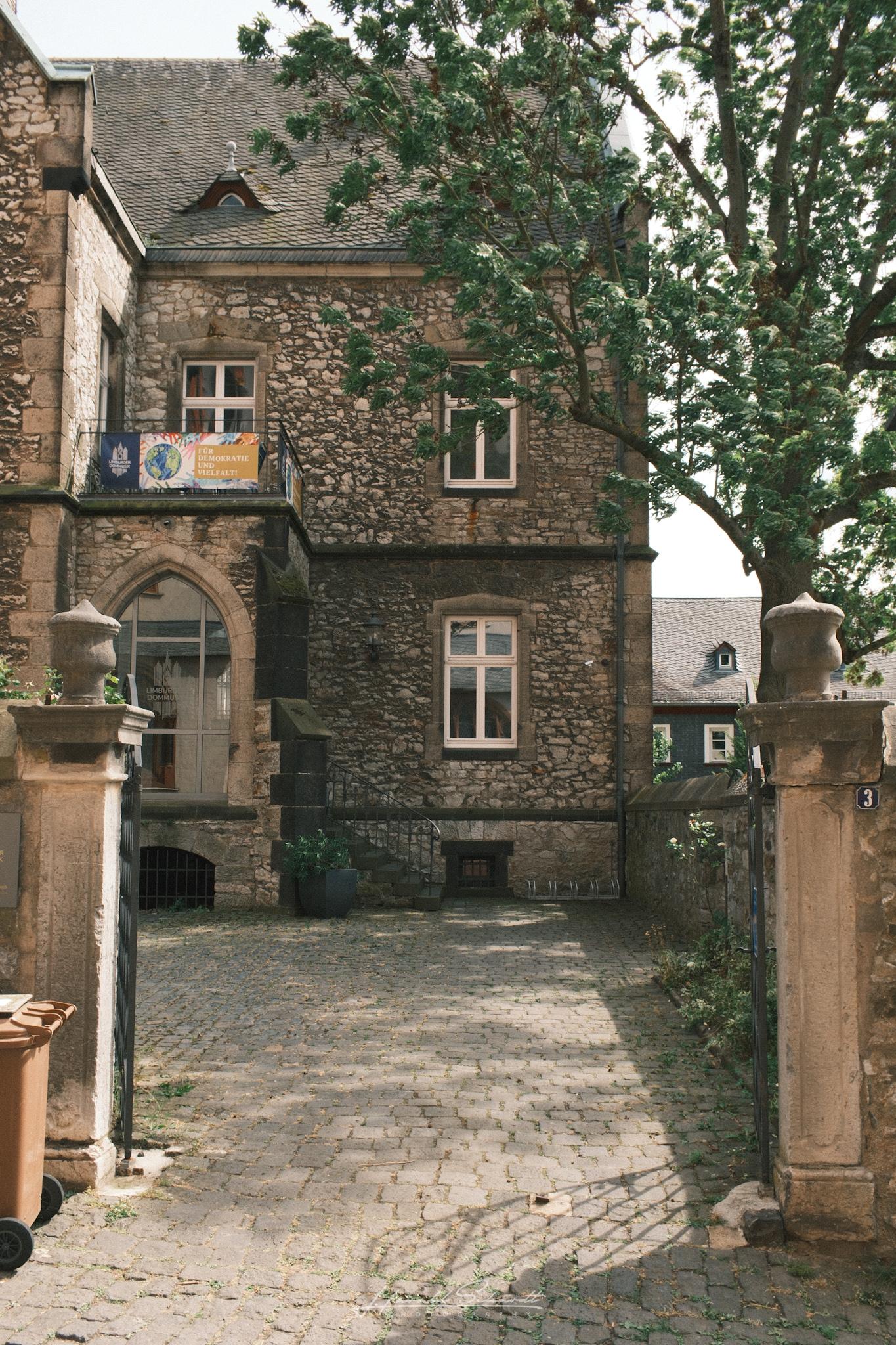 A historic stone courtyard beside the cathedral, framed by old buildings and trees.