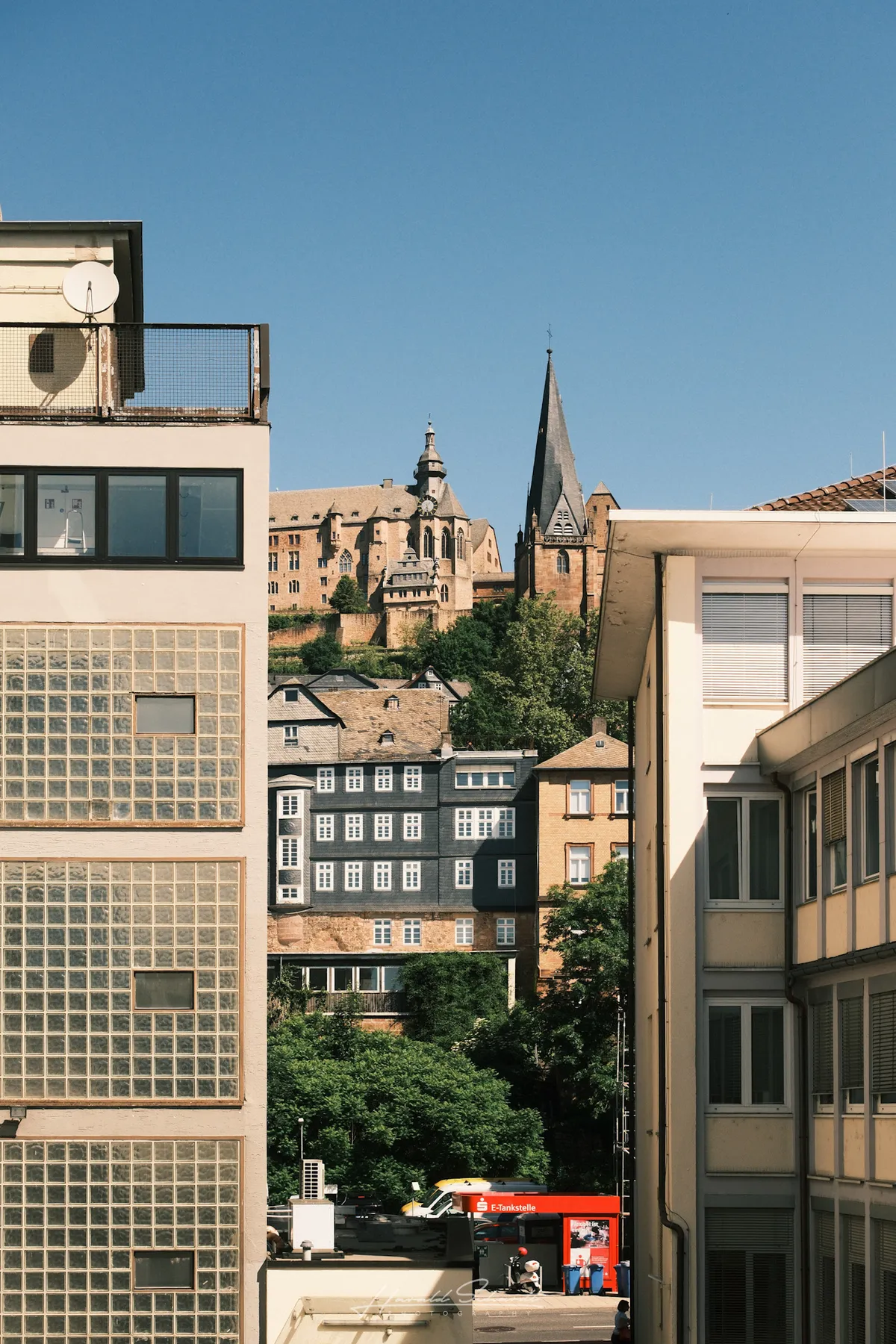 Marburg's Landgraf castle and church tower visible between modern buildings, framed against a clear blue sky.