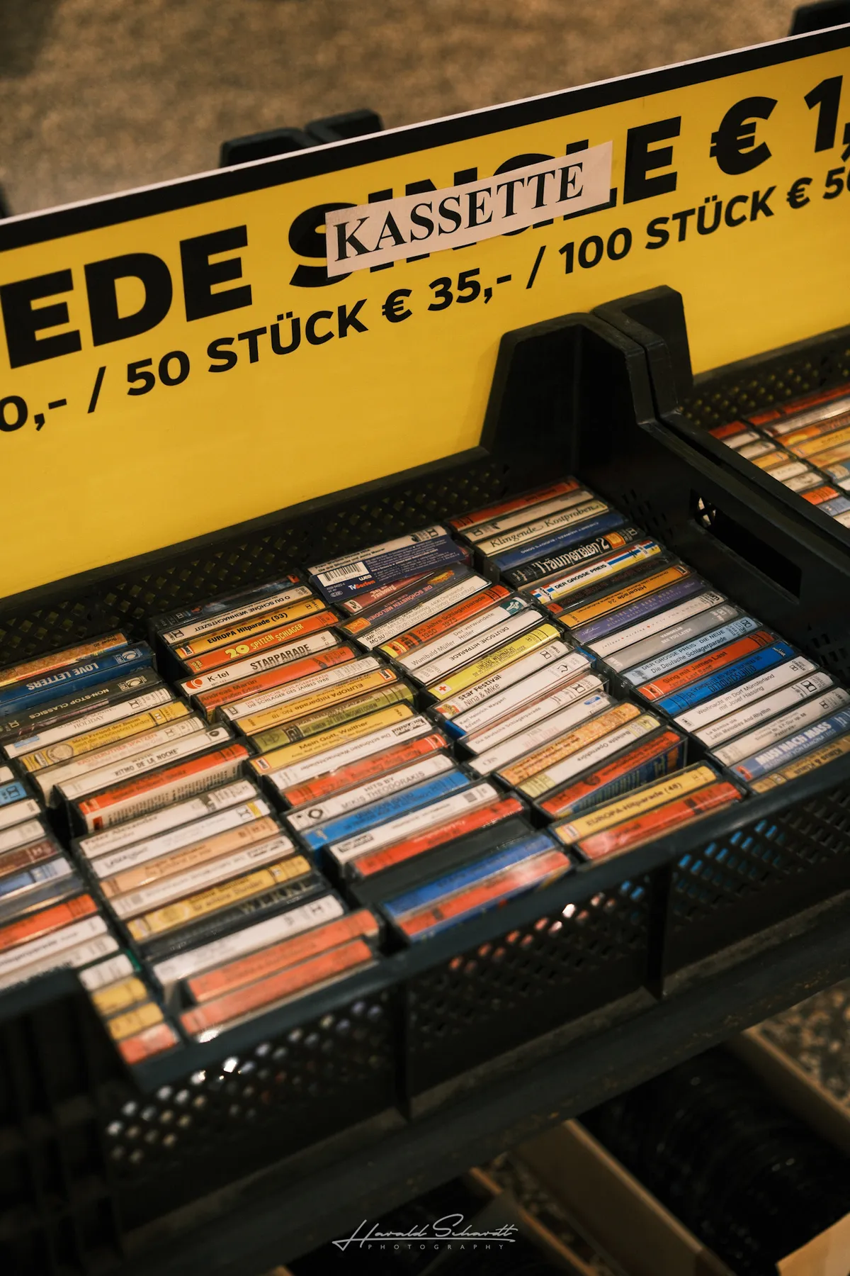 A crate of cassette tapes for sale under a yellow sign reading
