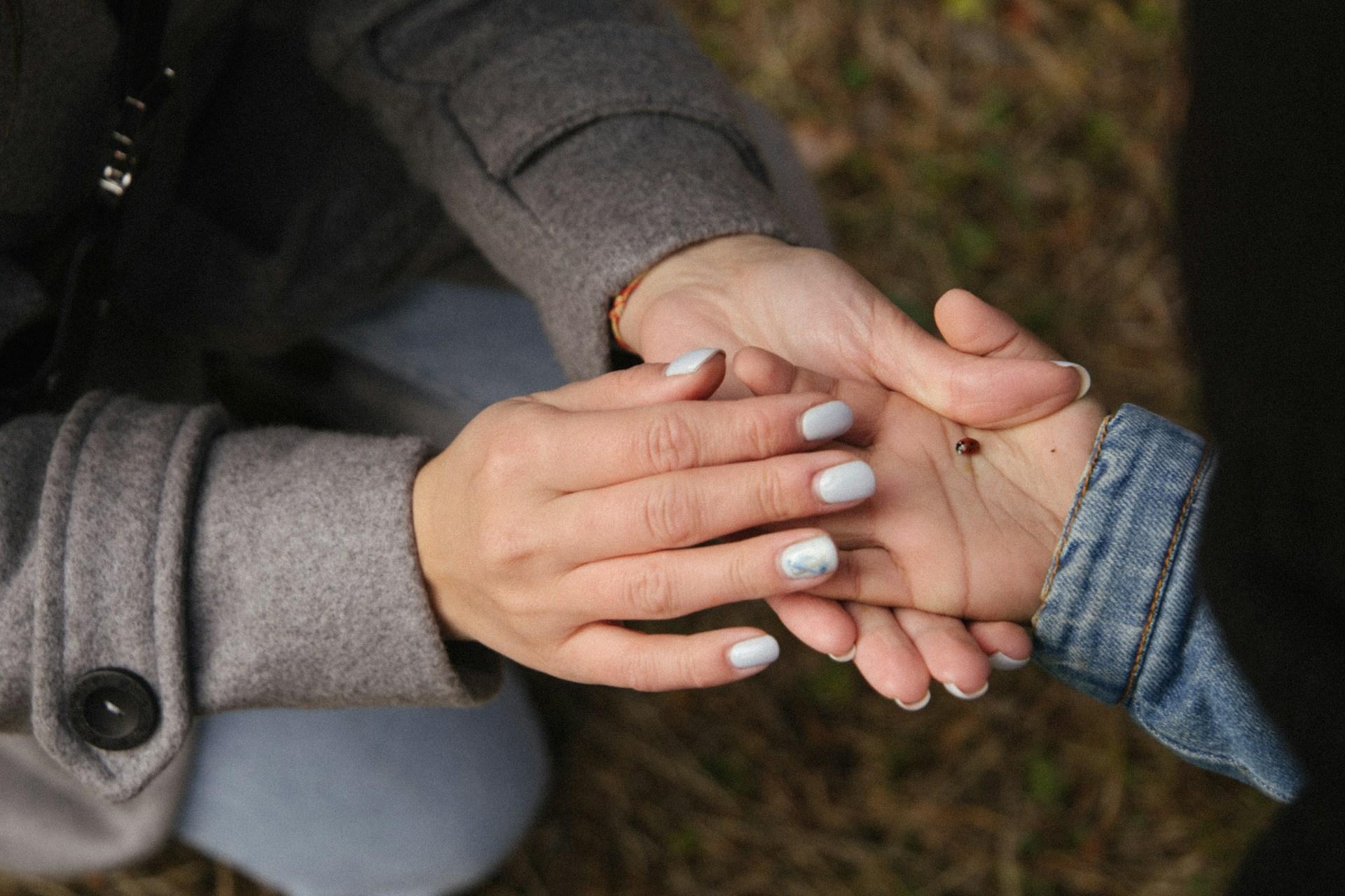 A mother gently holding her child’s hand with a ladybug resting on the palm.