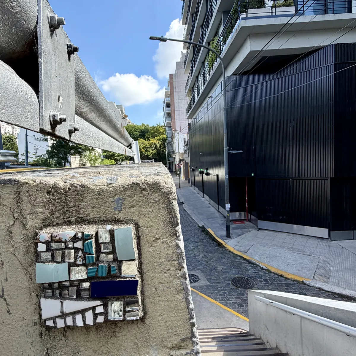 Some little square mirror installed on a wall but also some building, a narrow street and details you have to look for