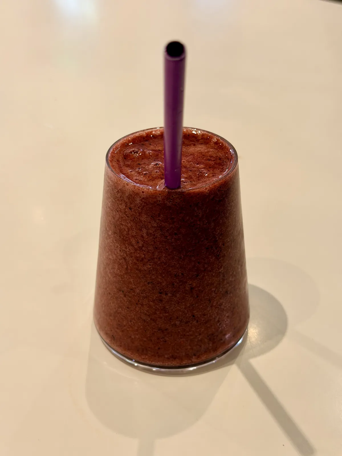 sort of a triangular shape glass over a white table with a redish beverage inside and a straw that you could say tries to get into the camera