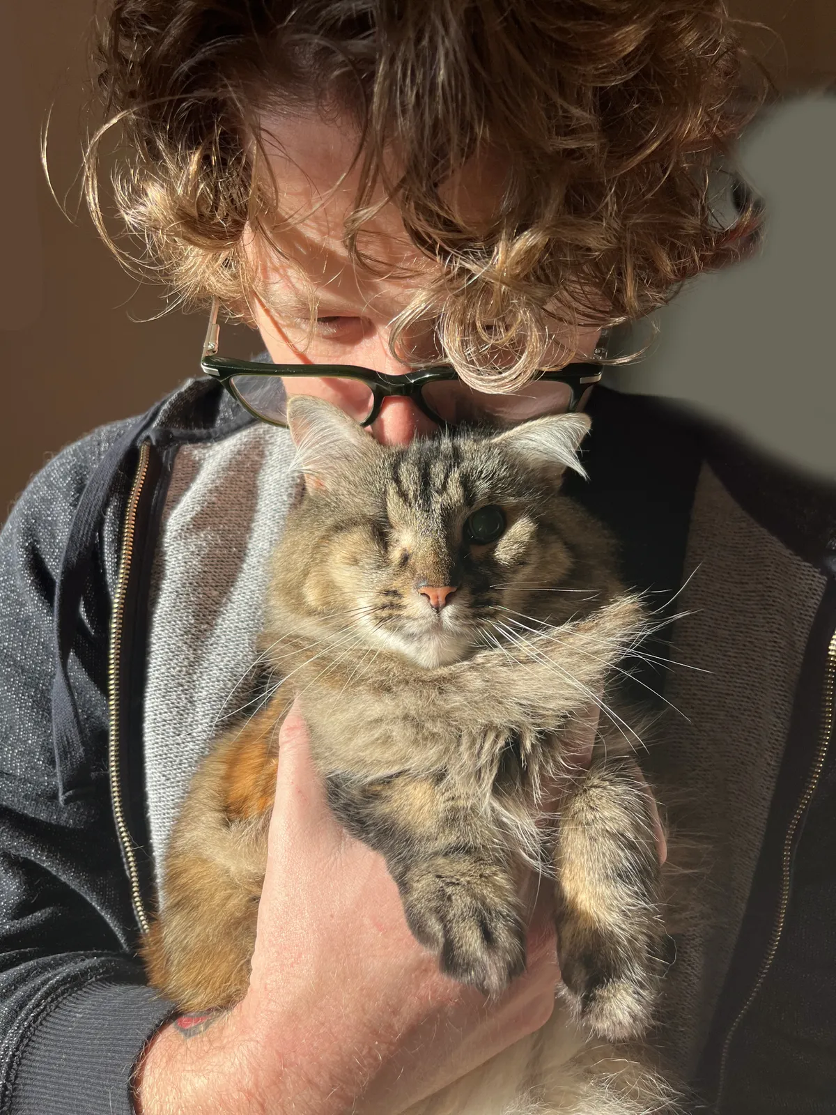 Man in glasses kissing one eyed cat