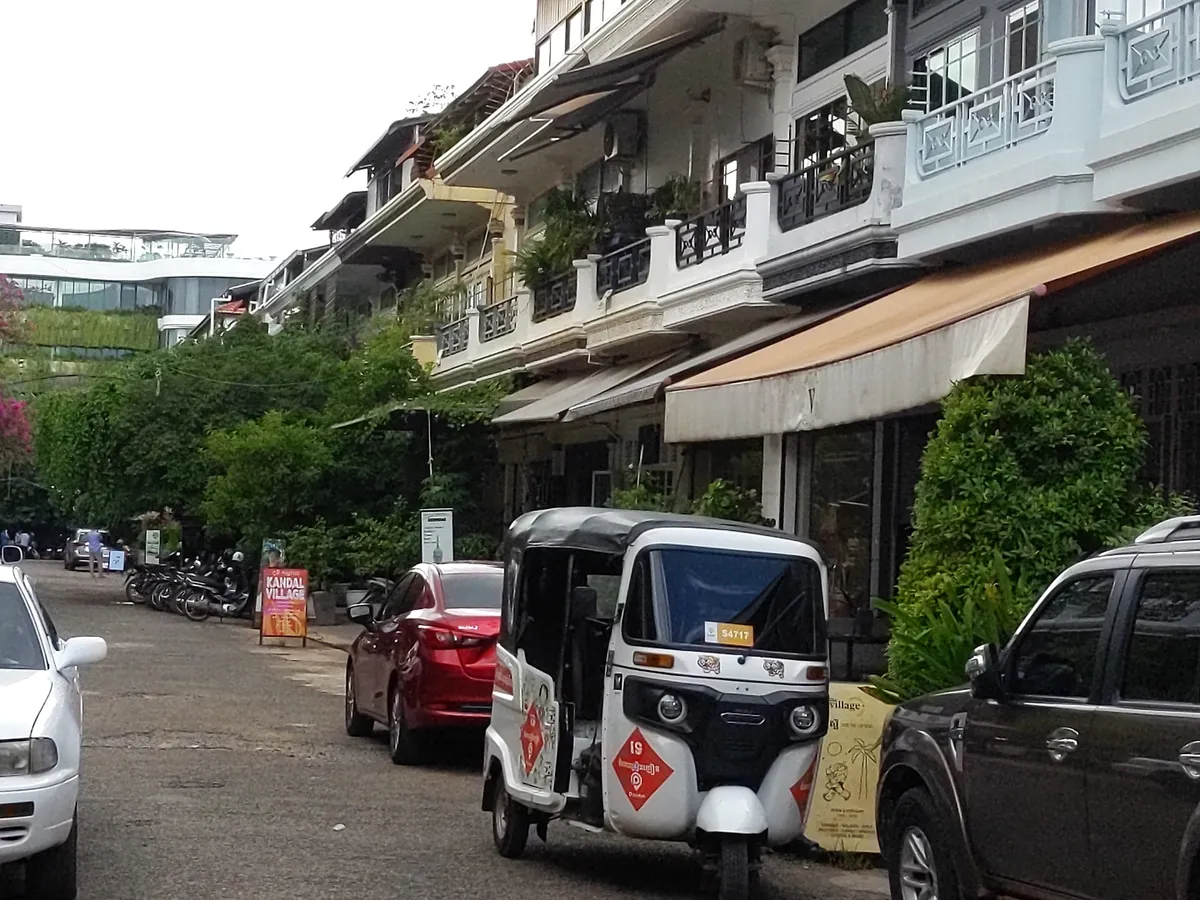 a sidestreet in an upscale neighborhood. apartments with terraces above and cafes on the ground floor. a lone tuk tuk waits for passengers on the street.