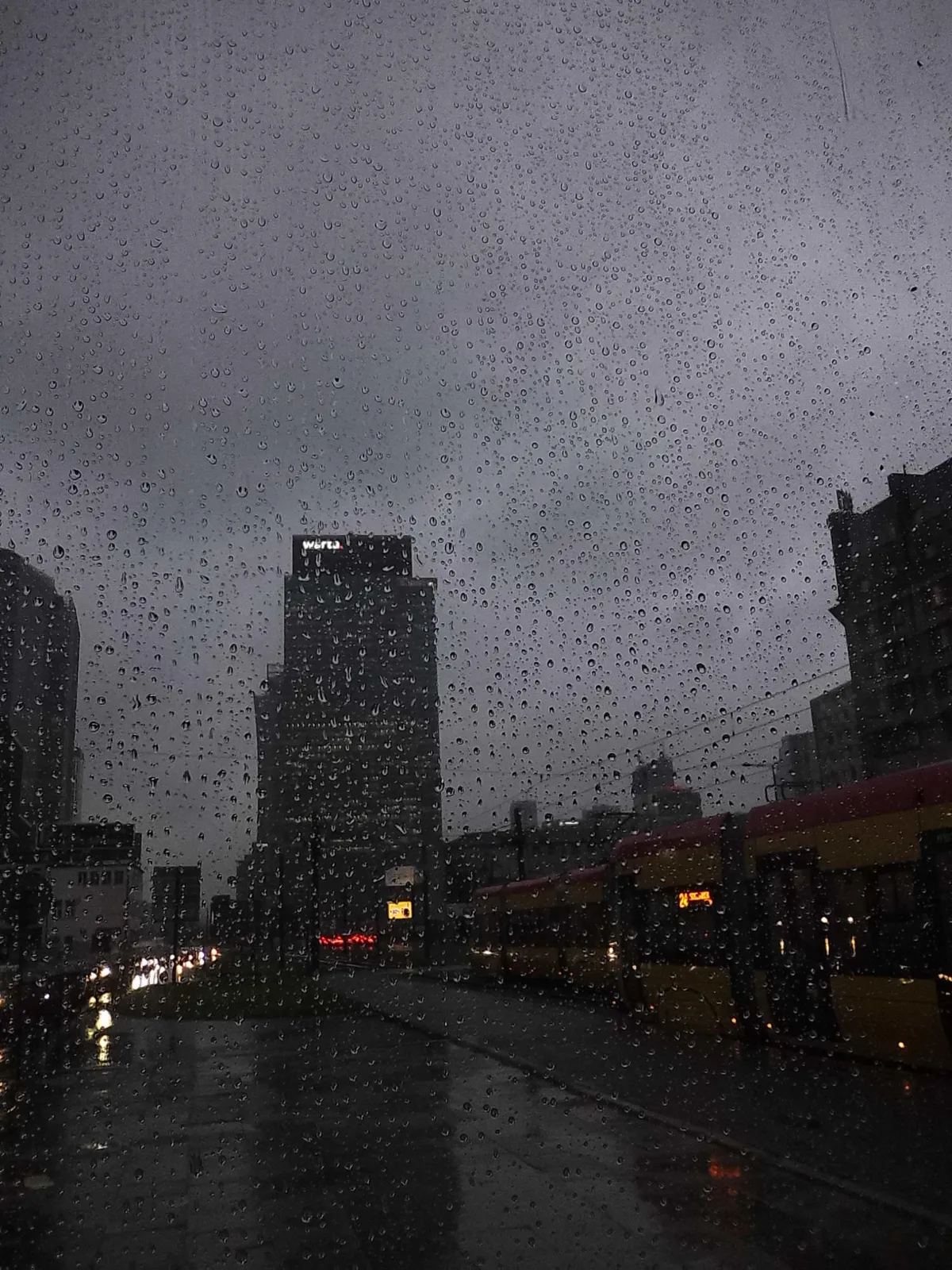 Warsaw, tram and some office buildings behind a wall of rain droplets (why am I feeling nostalgic for standing under a tram stop shelter in the rain)