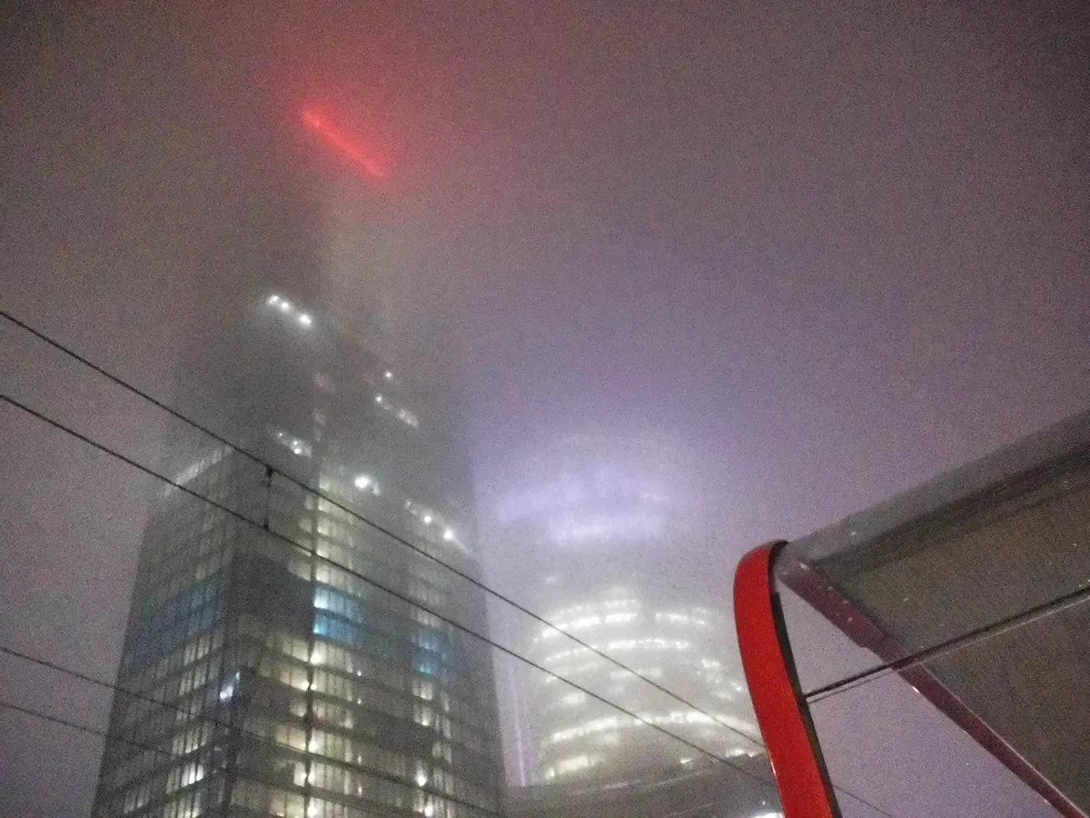 another view up from a tram stop shelter, but foggy as hell, smoothly blurring the text projected onto the Warsaw Spire and the sign atop the other skyscraper next to it