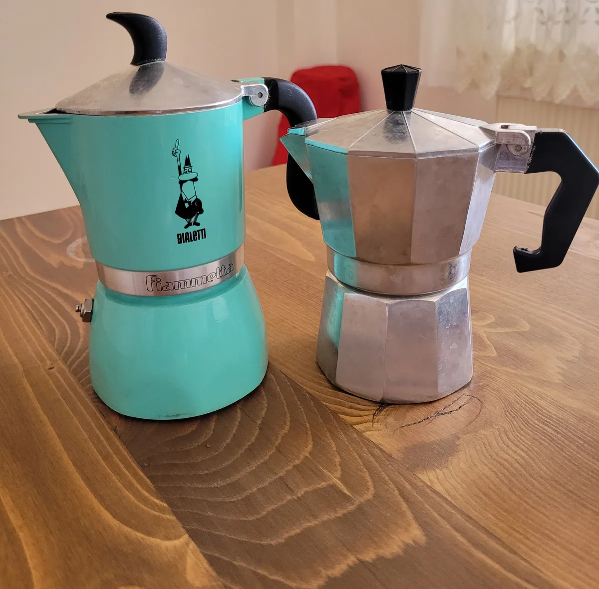 image of two moka pots, one turquoise and one made from shiny metal on a wooden desk